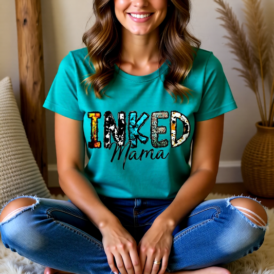 Woman wearing a teal t-shirt with 'Inked Mama' text, sitting on a couch.