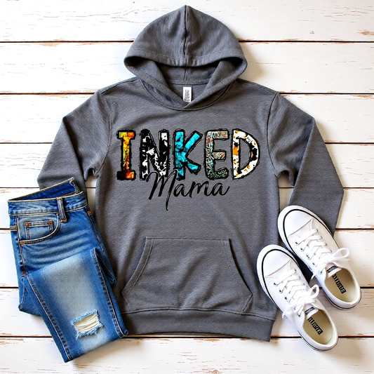 Gray hoodie with 'INKED Mama' text, blue jeans, and white sneakers on a wooden surface
