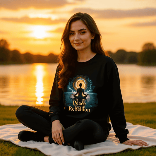 Peace Is My Rebellion™ | Karma & Grace™ — Model seated by a glowing lakeshore at golden hour, soft sunlight illuminating the black crewneck and metallic lettering with calm reflection